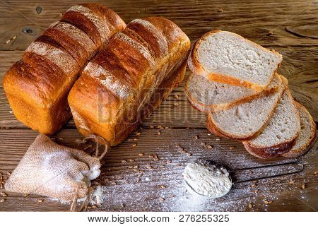 Two Black Breads Lie On A Wooden Table. Around The Sieve Flour Scattered. Slices Of Bread Are Near