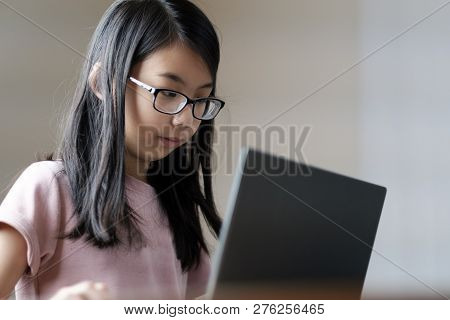 Young School Asian Girl With Eyeglasses Using A Laptop Hor Home Work.