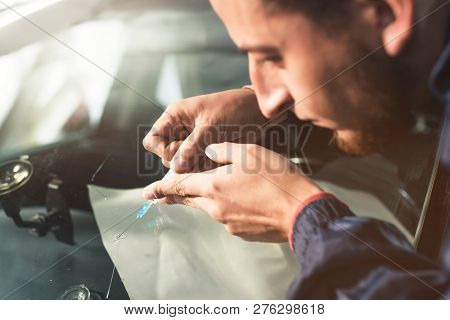 Close-up Of A Professional Windshield Repairman Fills A Crack In The Glass With A Special Polymer Th