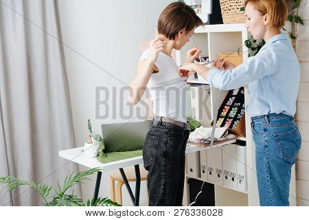 Young Female Fashion Designer Taking Measurements Of A Woman To Design New Clothes. They Both Have S