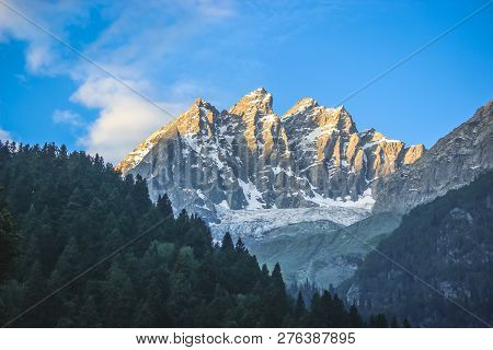 Sunrise On A Snow-capped Mountain Peak. A Mountain With A Glacier And A Pine Forest In The Foregroun