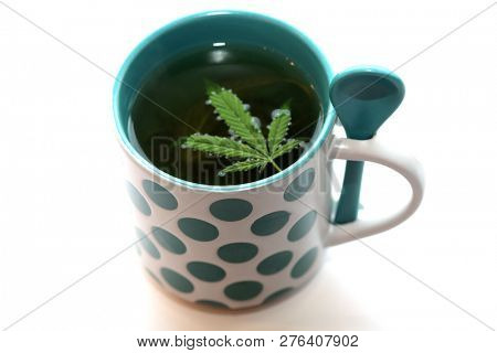 Hemp Tea. Marijuana Tea in a Tea Cup with a Cannabis Leaf and a Stem with Leaves and Flowers. Isolated on white. Room for text. 