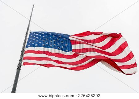 United States Flag Flying At A Half-staff Waving Against Gray Sky