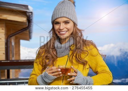 Woman drinking warm tea in the rustick wooden terrace on mountain, alpine view, snow on hills. 