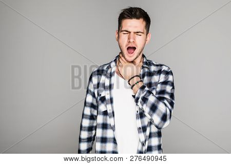 Young Man Having Sore Throat And Touching His Nec Against Grey Background.