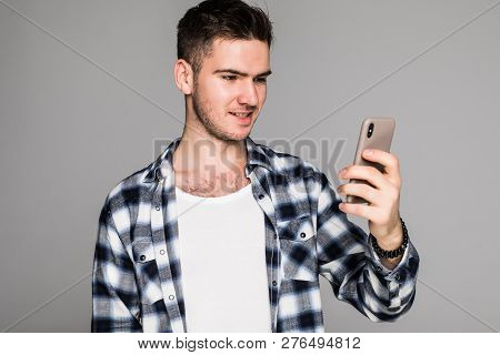 Portrait Of A Joyful Smiling Man In White Shirt Using Mobile Phone While Standing Isolated Over Whit