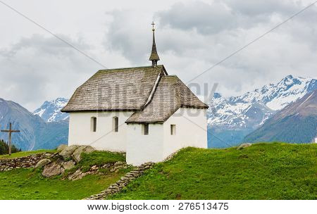 Lovely Small Old Church In Bettmeralp Alps Mountain Village, Switzerland. Summer Cloudy View.