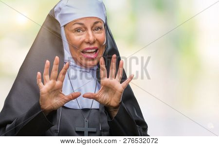 Middle age senior christian catholic nun woman over isolated background afraid and terrified with fear expression stop gesture with hands, shouting in shock. Panic concept.