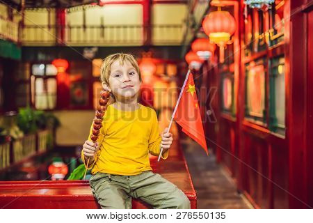 Enjoying Vacation In China. Happy Tourist Boy With A Chinese Flag And With Traditional Chinese Candi