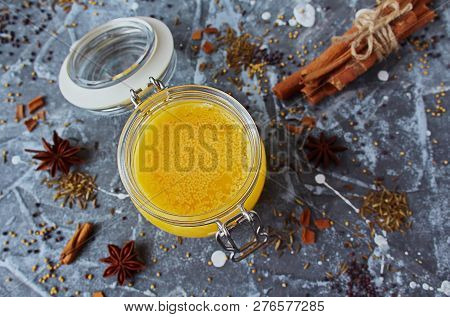 Ghee Oil In A Glass Jar. Spices: Yellow Mustard, Red Mustard, Cinnamon, Anise, Zira Seeds On A Grey 