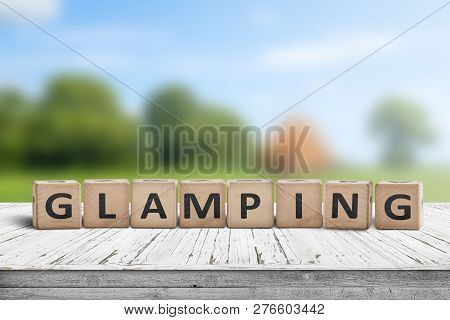 Glamping Sign On Wooden Planks In The Summer With A Green Camping Area In The Background