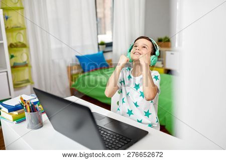 technology, gaming and people concept - boy in headphones celebrating victory in video game on laptop computer at home