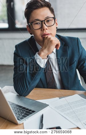 Young Kazakh Businessman In Eyeglasses Sitting At Wokplace And Looking At Camera