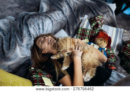 Funny Young Woman Having Fun With Little Puppy On A Sofa. Spend Together Winter Holidays, A Lot Of P
