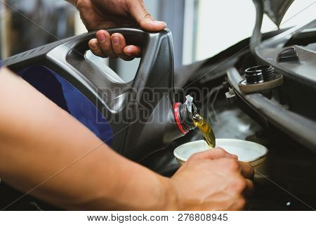 Mechanic Pouring Oil To Vehicle Engine. Serviceman Changing Motor Oil In Automobile Repair Service.