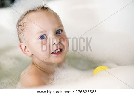 Little Boy With Blue Eyes In The Bath With Yellow Toy, In Bubbles Of Foam. Indoors, Left-sided