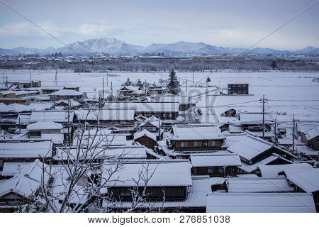 Early Morning Light Reflects Off Mountains In Distance From Small Japanese Village In Snow