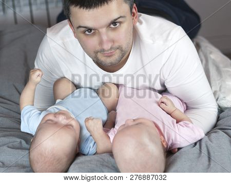 Young Father With His Newborn Twins Lying In Bed. Selective Focus