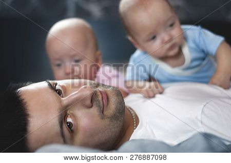 Young Father With His Newborn Twins Lying In Bed. Selective Focus