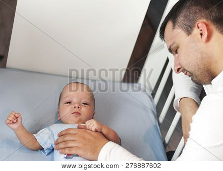Young Dad Is Tired Of Putting A Small Child To Bed. Dad And Son Fatherly Care Concept. Selective Foc