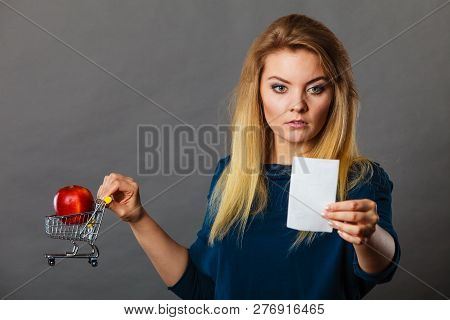 Worried Woman Holding Shopping Basket With Fruits Looking At Bill Receipt Being Scared Of Huge Price