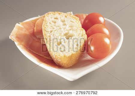 Dry Spanish Ham, Jamon, Italian Ham, Chopped Layers With Bread And Cherry Tomatoes On A White Heart-