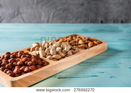 Compartmental Dish With Nuts On Blue Wooden Table. Hazelnut, Almond, Pistachio.