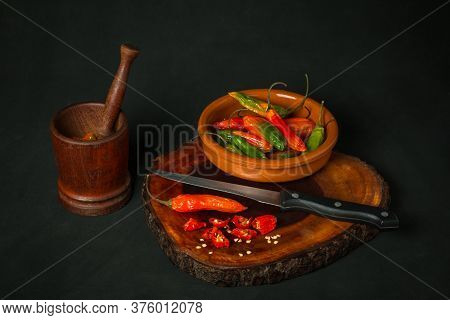 Still Life Of Hot Peppers In A Mortar Next To A Bowl And A Knife On A Dark Background