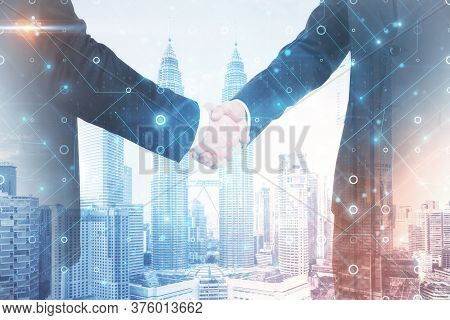 Businessmans Shaking Hands With Glowing Abstract Circuit Hologram On Blurry City Backround. Teamwork