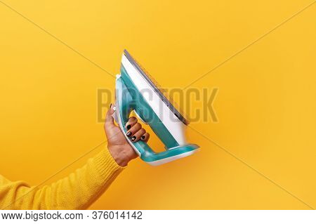 New Modern Iron In Hand Over Yellow Background