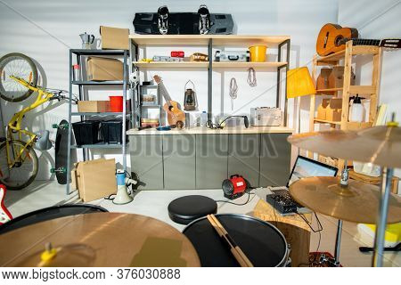 Interior of large contemporary garage for rehearsals with drum kit, acoustic guitar, bicycle and shelves with worktools and household stuff