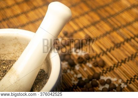 Ground Black In A Ceramic Mortar And Black And Coarse Salt Scattered On A Reed Mat. Close Up.