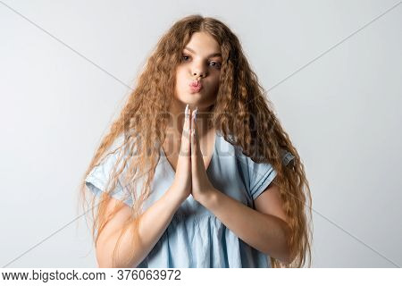 Please, Help Me. Emotive Pleased European Girl With Curly Long Hair, Keeps Hands In Praying Gesture,