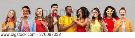 photo booth and fun concept - happy smiling people with party props over grey background