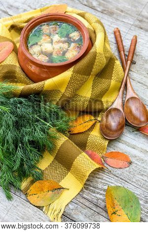 Soup With Croutons And Dill In A Clay Pot Wrapped In A Checkered Yellow Scarf For Warmth And Strewn 