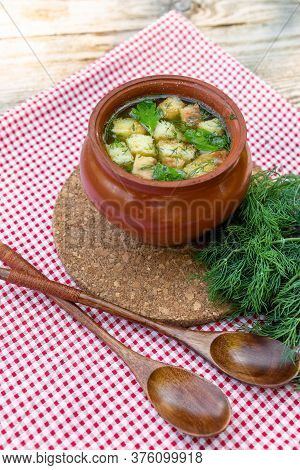 Hot Soup In A Clay Pot With Croutons And Herbs On A Stand And A Red Checkered Napkin. Vegetarian Sou