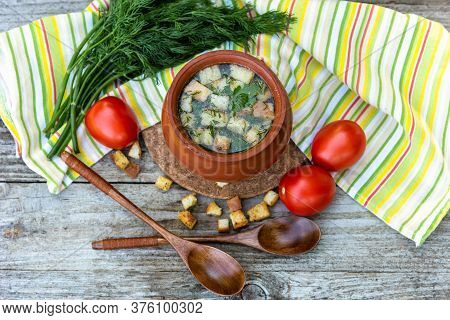 Delicious Soup With Croutons, Dill, Tomatoes In A Clay Pot At Home On A Yellow Napkin Background.