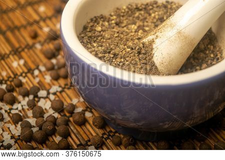 Ground Black In A Ceramic Mortar And Black And Coarse Salt Scattered On A Reed Mat. Close Up.
