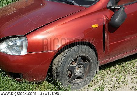 Part Of A Red Broken Passenger Car With A Broken Mirror And A Black Wheel On The Street