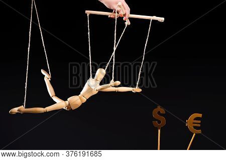 Cropped View Of Puppeteer Holding Wooden Marionette On Strings Near Currency Signs Isolated On Black