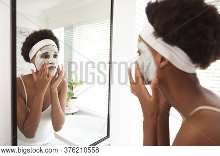 Mixed race woman spending time at home self isolating and social distancing in quarantine lockdown during coronavirus covid 19 epidemic, taking care of her skin in her bathroom.