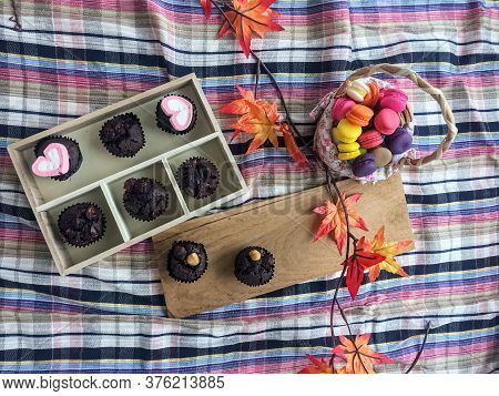Top Vier Of Chocolate Cupcake And Magaroon Put Beside Dried Maple Leaf,on Colorful Table Cloth.