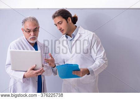 Experienced doctor teaching young male assistant using computer