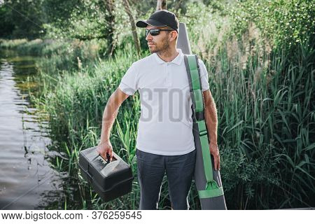 Young Fisherman Fishing On Lake Or River. Cool Busy Confident Guy Walking With Fishing Equipment Bes