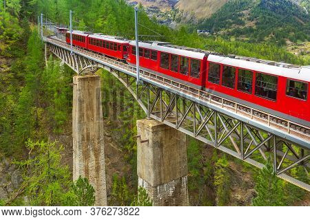 Zermatt, Switzerland. Gornergrat Red Tourist Train Close-up On The Bridge In Swiss Alps