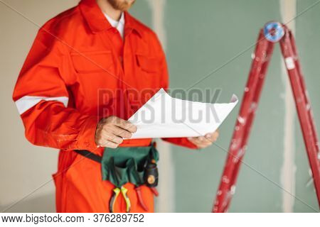Close Up Foreman In Orange Work Clothes And Yellow Hardhat Holdi
