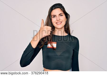 Young beautiful girl wearing Hello my name is sticker over isolated background happy with big smile doing ok sign, thumb up with fingers, excellent sign
