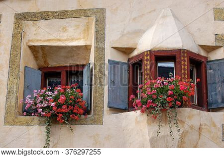 Old Balcony With Wooden Windows And Red Geraniums In The Ancient Village Of Ardez, Scuol Municipalit