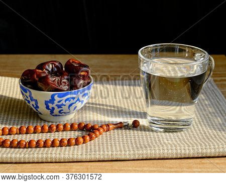 Cup With A Traditional Oriental Pattern With Dates, A Glass Of Clear Water, Stone Rosary On A Napkin