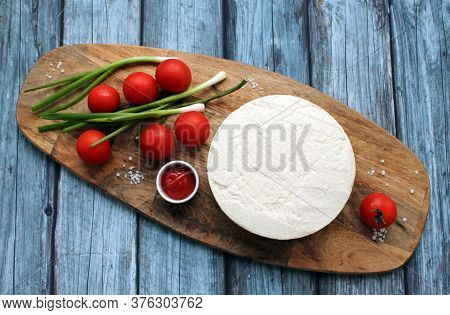 Homemade cheese made from goats milk, small tomatoes on a branch, red sauce lie on a wooden Board on